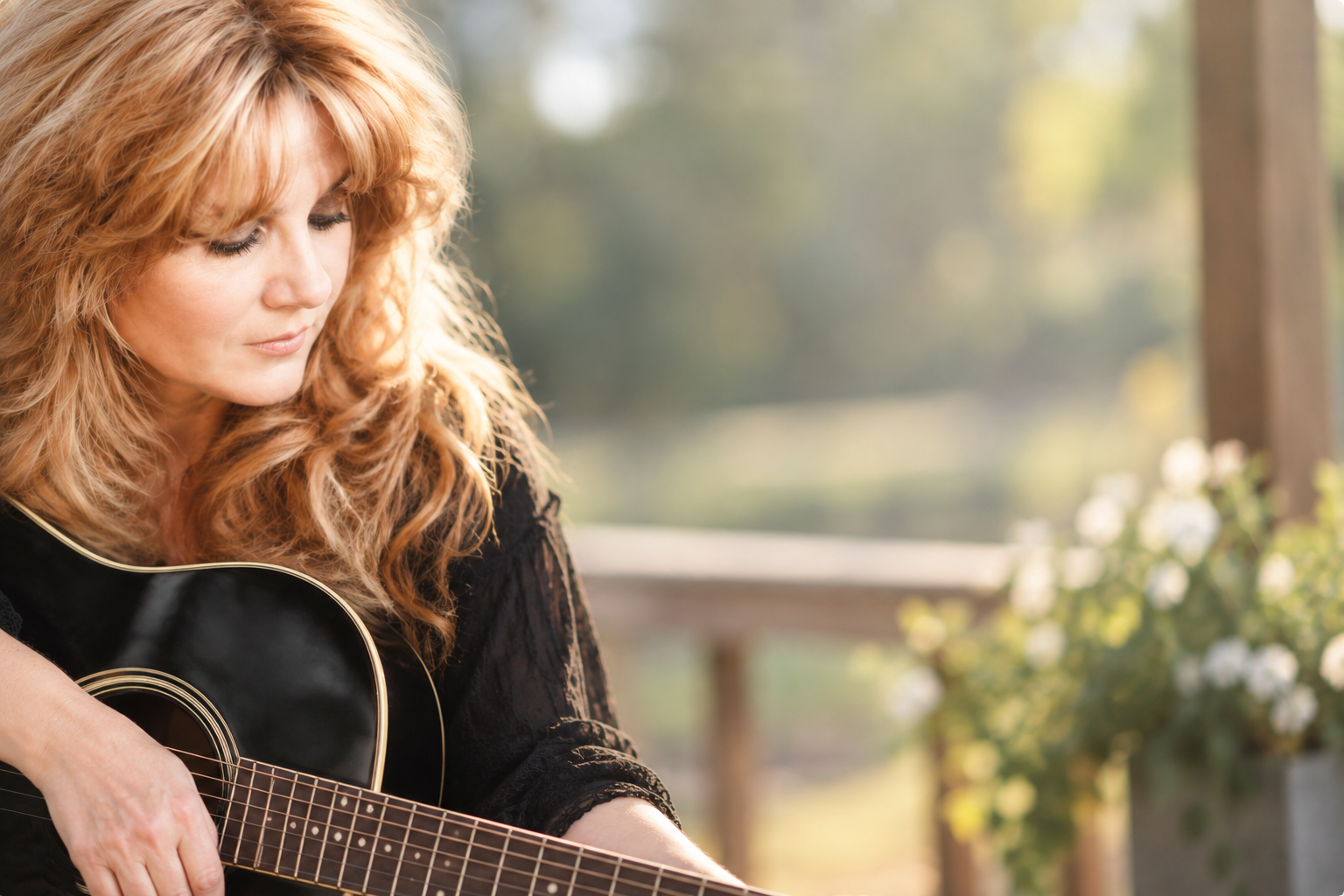 Keeli holding a black acoustic guitar beside flowers